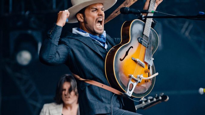 Canva - Man in Black Formal Suit Holding Electric Guitar While Raising His Right Hand and Opening His Mouth in Tilt Shift Lens Photography